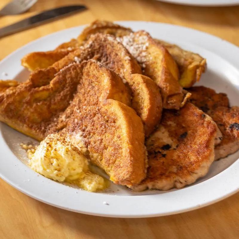 A stack of French toast dusted with sugar, served with scrambled eggs